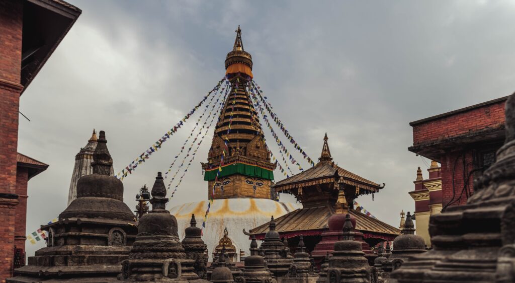 Ancient Swayambhunath Stupa in Kathmandu with vibrant prayer flags under cloudy sky.