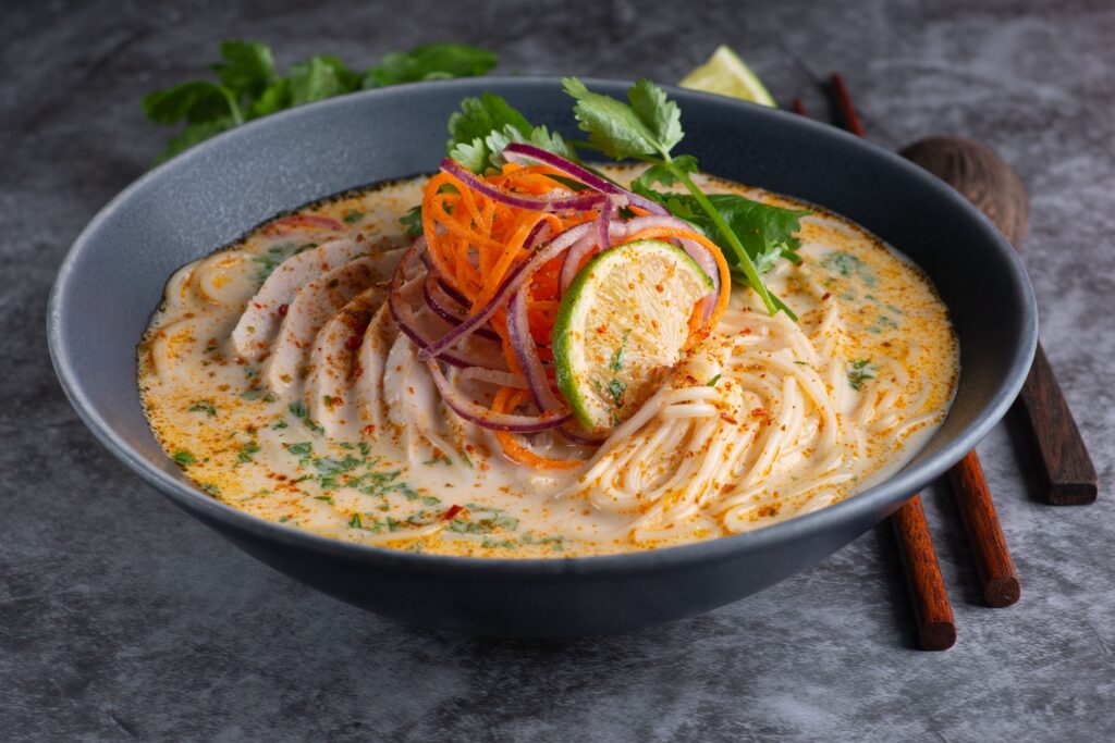 Delicious creamy noodle soup garnished with vegetables and spices. Perfect fusion dish for food lovers.