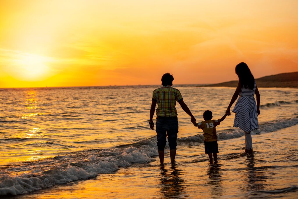A family walks on an Indian beach during a vibrant sunset, holding hands.