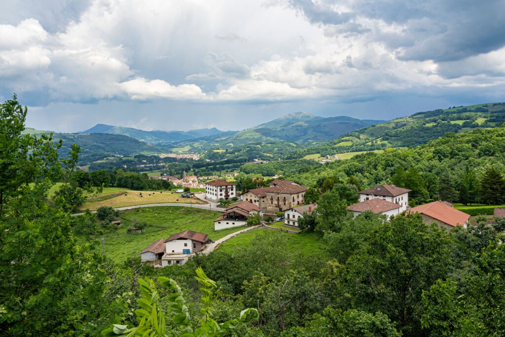 Charming village nestled in a lush green valley under dramatic skies, showcasing summer beauty.
