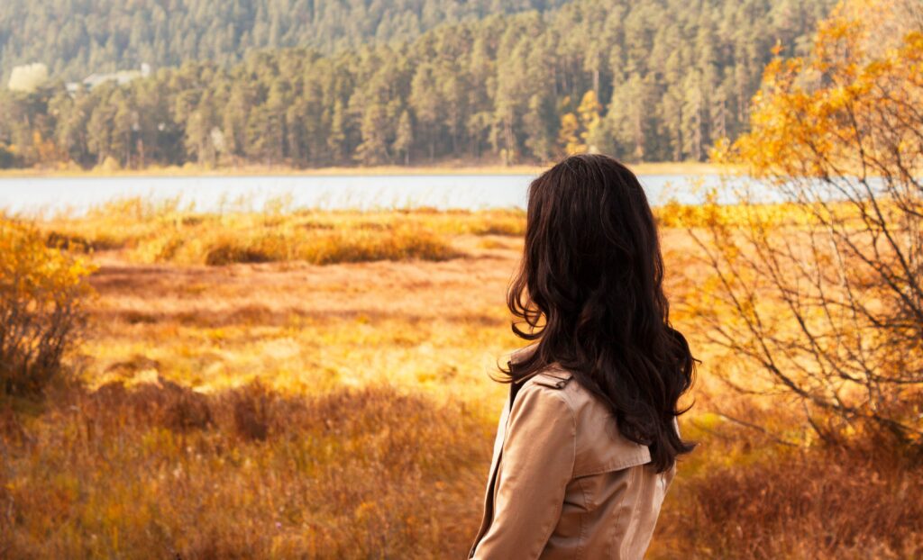 Woman in autumn landscape looking at serene lake, surrounded by colorful fall foliage.