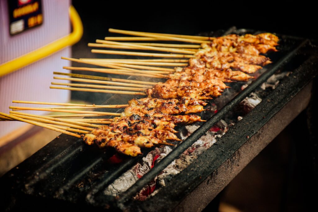 Close-up of chicken satay skewers grilling over charcoal, showcasing street food delicacy.