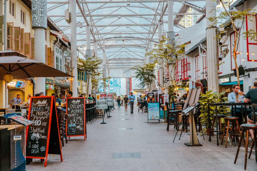A vibrant street dining area with people enjoying meals, surrounded by modern architecture and signage promoting local offers.