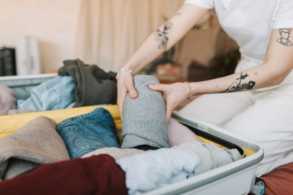 Close-up of a person packing clothes into a suitcase, showing arm tattoos, in a cozy indoor setting.
